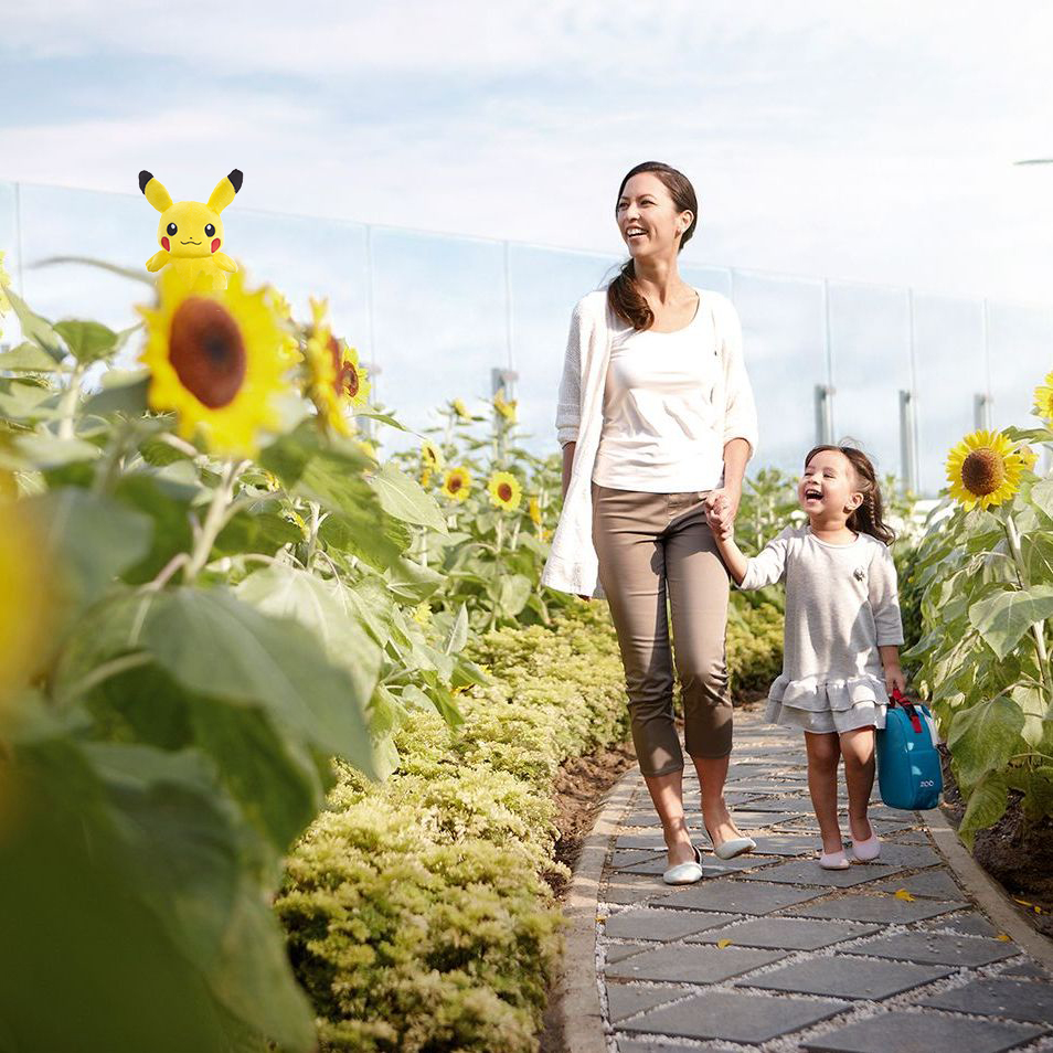 A mother and daughter smiling as they walk down a path in a field of sunflowers